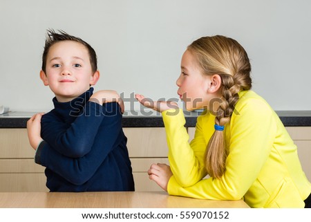 A pretty little girl blows a hand kiss to her cute brother at home in the kitchen
