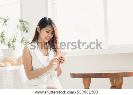 Happy Asian woman smiling while using smart phone in white room