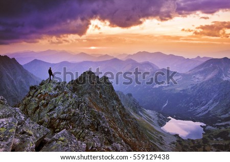 Tourist stand on the top of big mountains and looking to the valley and sky with clouds and beautiful sunset light. Wallpaper with space for your montage - aim, top, business, thinking concept photo Royalty-Free Stock Photo #559129438