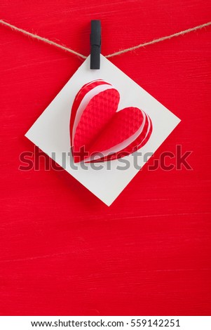 White gift card wth paper hearts hanging on the rope on red wooden background. Vertical orientation, place for copyspace.