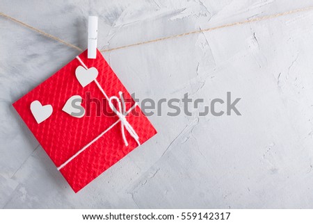 Red gift card with white paper hearts hanging on the rope on gray concrete background. Horizontal orientation, place for copyspace.