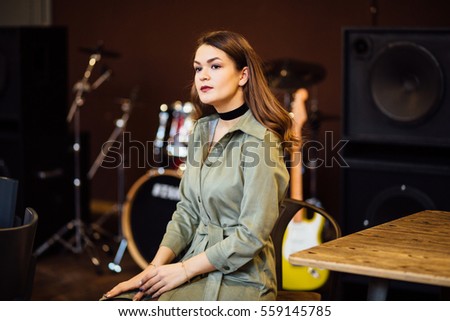Beautiful woman in stylish dress posing in front of music instruments in loft interior.