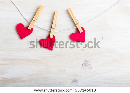 Three red paper hearts hanging on string with mini clothes pin over white wooden board. Top view with copy space