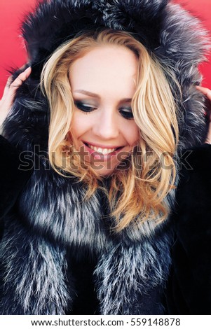 Outdoor portrait of young beautiful fashionable woman wearing stylish winter fake fur coat and furry hood. Photo toned style instagram filters.