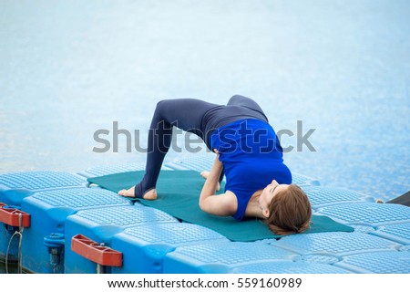 Young woman doing yoga by the lake, located on the docks. 
Concept healthy lifestyle. Lots of copy space. 
