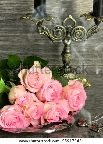 A bouquet of pink roses on a silver tray in smoke from a candelabra