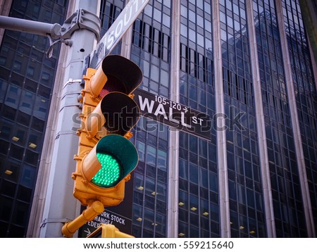 View on wall street yellow traffic light with black and white pointer guide. Green traffic light to Wall street banks money dollars finance offices. New York traffic light on Wall street money