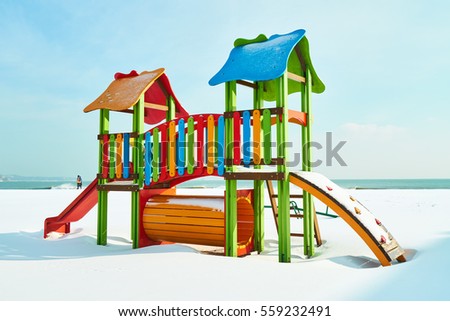 Bright children's playground in the snow on the beach in winter sunny day
                               