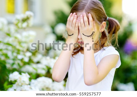 Cute little girl covering her face with her hands on summer day. Sad child with eyes pictured on her palms. 