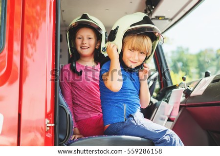 Two cute kids playing in fire truck, pretending to be firefighters, open doors day at fire station. Future profession for children. Educational program for schoolkids Royalty-Free Stock Photo #559286158