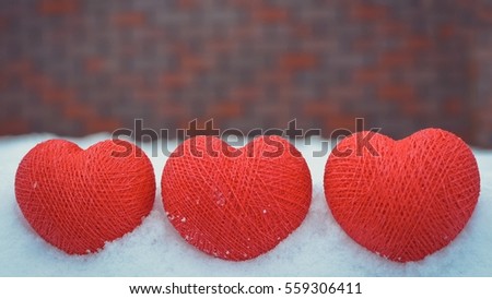 Three red cotton hearts in the snow on the background of brick wall. Front view. Copy space.