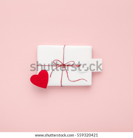 Valentine or birthday white gift with red bow,  blank label decorated with felt heart on pink background. Valentines day. Flat lay. Copy space.