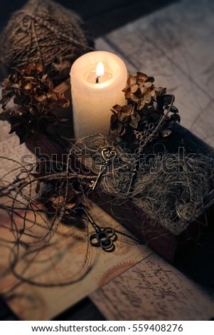 vintage composition with burning candle, old keys, dry flowers, ball of thread on table. nostalgia mood. magic ritual, witchcraft