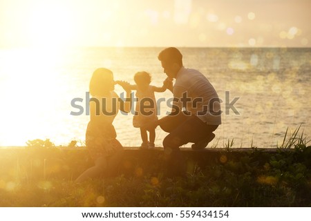Silhouette of Asian family outdoor activity, enjoying holiday together on seaside in beautiful sunset during vacations.