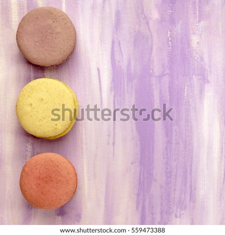 A photo of three macarons, shot from above on a light purple background texture, with copy space
