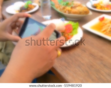 Blurry hand of Asia man using smartphone taking food on wooden table