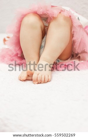 Photo of baby girl's legs. Little girl in a pink dress lying on white soft blanket 
