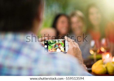 Three beautiful women posing for a photo around a terrace table by a summer evening. Focus on the smartphone. Shot with flare