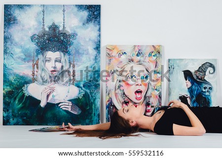 Beautiful female artist at Picture canvas on white background. Girl painter with brushes and palette. Art creation concept. Lying on the floor against the backdrop of real paintings.