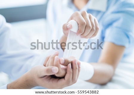 Close-up doctor is bandaging upper limb of patient. Royalty-Free Stock Photo #559543882