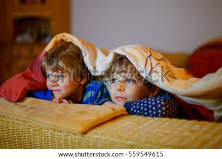 Happy little brothers, adorable kid boys watching television while lying. Funny children enjoying cartoons. Cute preschool siblings having fun together.