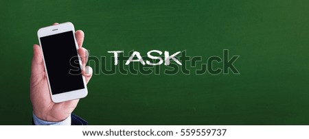 Smart phone in hand front of blackboard and written TASK