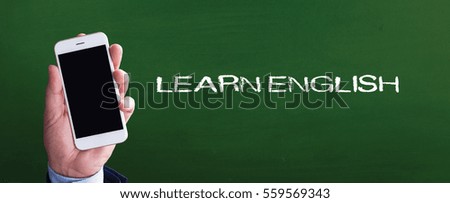 Smart phone in hand front of blackboard and written LEARN ENGLISH