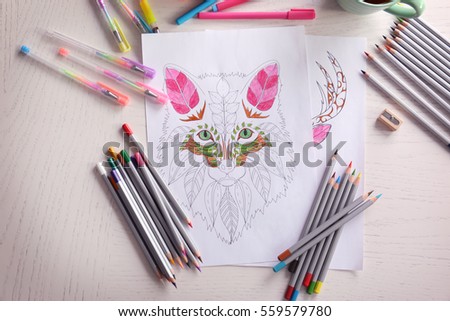 Composition of colouring picture, pencils and pens on wooden table