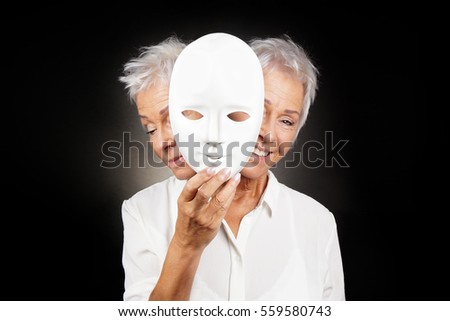 older woman hiding happy and sad face behind mask, concept for manic depression or bipolar or dramedy comedy drama Royalty-Free Stock Photo #559580743