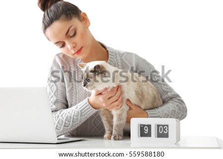 Beautiful young woman sitting at table with cute cat, on light background