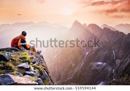 Young tourist, hiker with backpack siting on the top of the hill mountains and looking at beautiful summer sunset Royalty-Free Stock Photo #559594144