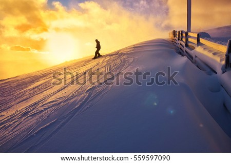 Snowboarder ride on the top of snowy hill in ski resort during calm winter sunset. Scenery of athlete - wallpaper with space for your montage Royalty-Free Stock Photo #559597090