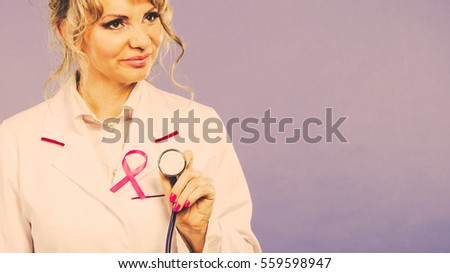 Breast cancer. Medical help treatment concept. Female blonde doctor in white medic apron with pink ribbon holding stethoscope. Filtered.
