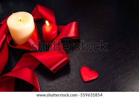 Burning candles, wrapped in red ribbon and hearts on Valentine's Day. Dark texture with a romantic symbol of love by 14 february.
