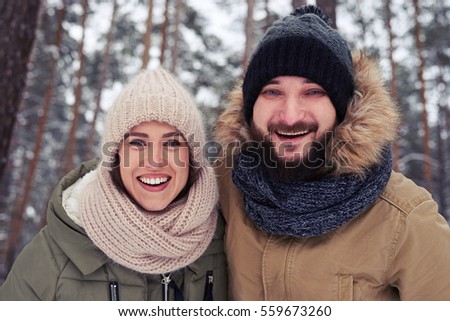 Low angle of happy couple standing in the wintry forest. Couple posing at the camera. Beautiful landscape of snow-capped branches of trees 