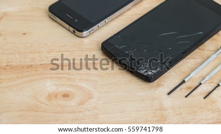 Damaged mobile phone and repairing tools on wooden desktop. Crashed smartphone repair service concept. There are two broken phones and three screwdrivers on the table