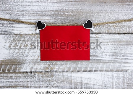 Blank red holiday sign hanging by black and white heart clips on rope against white painted rustic antique wood background; Valentine's Day, Christmas and love concept with white painted copy space