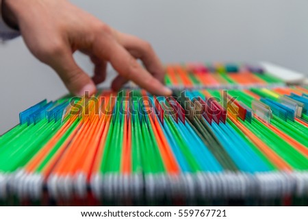Abstract background of colorful hanging file folders in drawer. Mans hand Search document. Stock photo