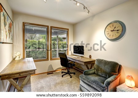 Gray and beige home office interior with rustic tables and comfortable gray velvet reading armchair atop taupe carpet floor. Northwest, USA
