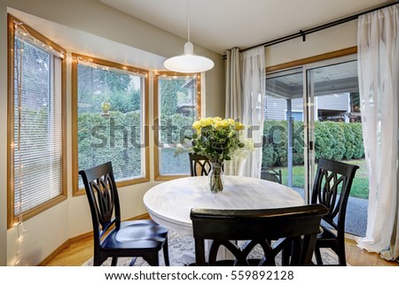 Dining room with curved window wall and glass sliding doors leading out to deck and yard.  Round white washed dining table lined with black chairs and topped with fresh yellow roses . Northwest, USA