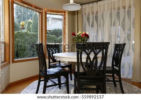 Dining room with curved window wall and glass sliding doors leading out to deck and yard.  Round white washed dining table lined with black chairs and topped with fresh roses . Northwest, USA