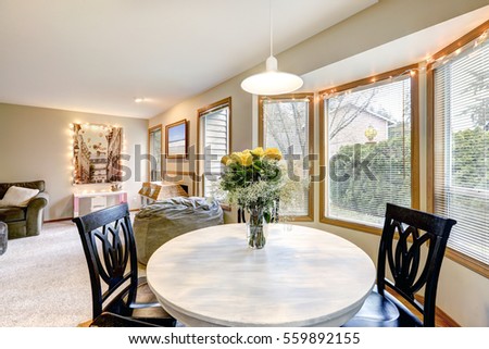 Dining room with curved window wall, Round white washed dining table lined with black chairs and topped with fresh yellow roses . Northwest, USA