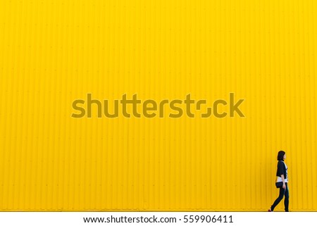 Woman walks near yellow wall, copy space background