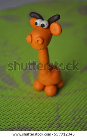 Cute little giraffe from plasticine on a background of green leaves. Baby safari