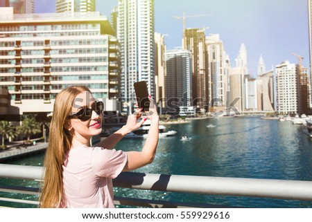 Blonde lady raises her hand with iPhone to take a picture of skyscarapers in Dubai