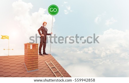 Young caucasian businessman standing on house roof presenting green construction. Mixed media