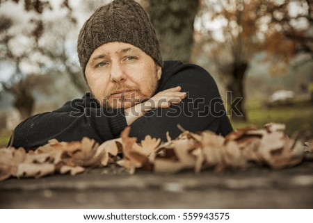 Close up portrait pensive man with wool hat sitting on a bench in the park in autumn