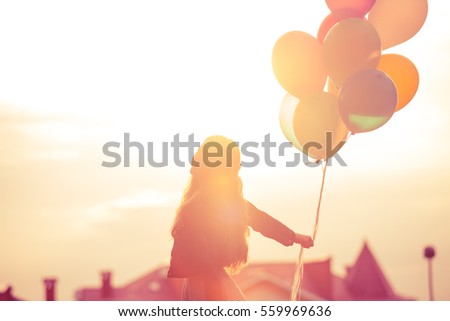 Pretty girl with big colorful balloons walking on the hills near the town. Focus on balloons