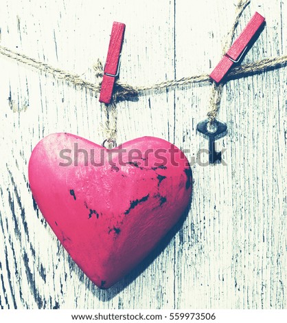 Decorative red heart and small metal key on a rope against the background of an old white board, close up. Festive romantic image for Valentine's Day
