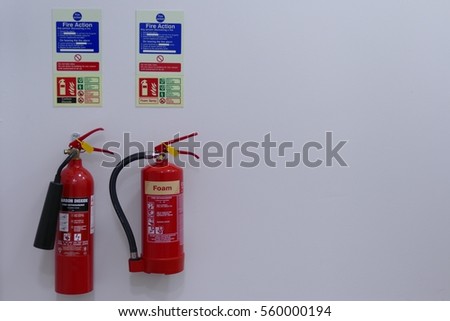 Fire equipment with white background: Two extinguishers attached onto a wall with two signs stating the fire action.